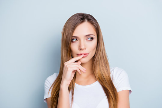 Portrait of mysterious thoughtful girl touching lips with finger isolated on grey background looking to the side with eyes
