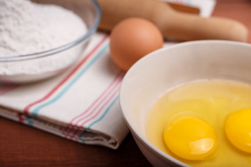 pizza or pie recipe ingridients, food flat lay on wood kitchen table background. baking ingredients. Bowl, eggs, milk, flour, eggbeater, rolling pin and eggshells