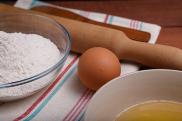 pizza or pie recipe ingridients, food flat lay on wood kitchen table background. baking ingredients. Bowl, eggs, milk, flour, eggbeater, rolling pin and eggshells