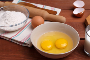 pizza or pie recipe ingridients, food flat lay on wood kitchen table background. baking ingredients. Bowl, eggs, milk, flour, eggbeater, rolling pin and eggshells