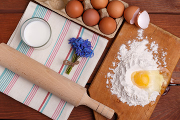 pizza or pie recipe ingridients, food flat lay on wood kitchen table background. baking ingredients. Bowl, eggs, milk, flour, eggbeater, rolling pin and eggshells