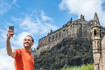 A happy young man tourist taking selfie at Edinburgh Castle with mobile phone.
