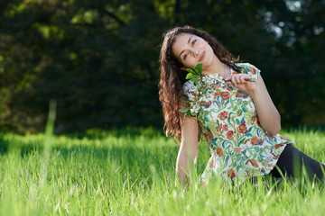beautiful girl sitting on a glade in the park, bright sun and shadows on the grass