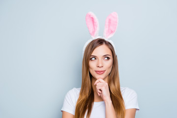 Portrait of playful thoughtful girl wearing bunny ears holding hand on chin looking to the side...