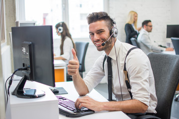 Beautiful handsome man with headset showing thumb up while working in call center.