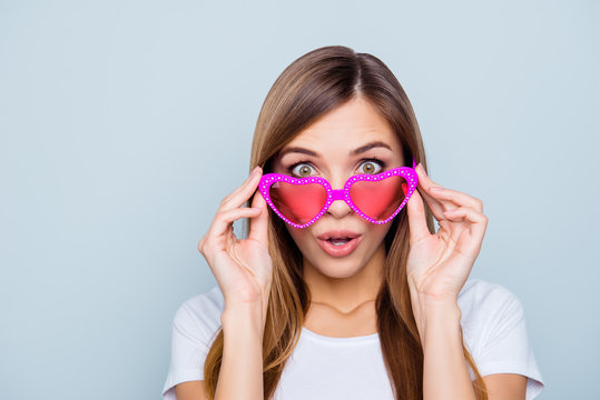 Portrait of shocked frustrated girl looking out pink glasses in heart shape with wide open eyes mouth isolated on grey background