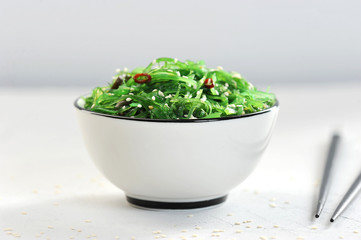 Salad chuka from seaweed in a white bowl. Salad sprinkled with sesame seeds. In the frame,...