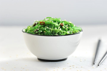 Salad chuka from seaweed in a white bowl. Salad sprinkled with sesame seeds. In the frame, chopsticks. Light background. Close-up. Macro photography.