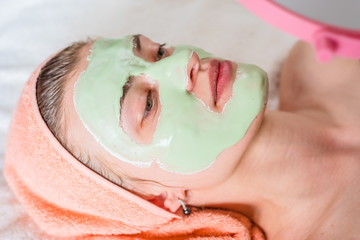 Fototapeta premium Young woman lying with a towel on his head and cosmetic algae mask on her face - beauty treatment close-up