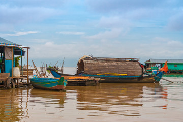 A wooden sampan-like boat with a curved roof tied up to a floating house in Chong Kneas, the...