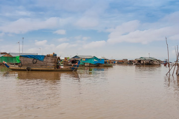 Fototapeta na wymiar View of the floating houses in Cambodia's floating village Chong Kneas on Tonle Sap Lake. On the left is a wooden sampan-like boat including a small shelter with a curved roof anchored.