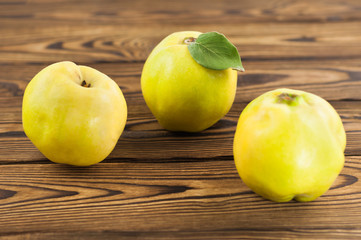 Scattered three whole fresh ripe quinces on old weathered rustic brown wooden table
