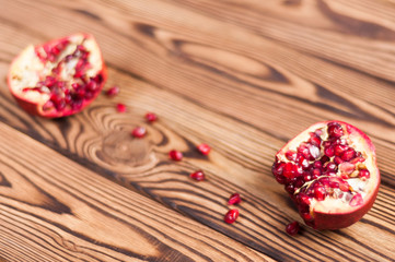 Scattered fresh ripe red seeds of pomegranate near two half pomegranate on old brown weathered wooden planks