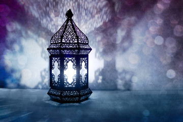 Ornamental Arabic lantern with burning candle glowing at night and glittering blue bokeh lights....