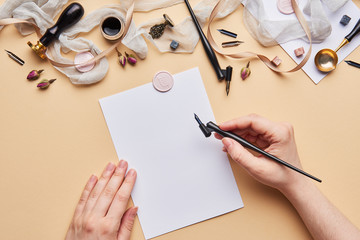 Flat lay of feminine desk workspace with female hands. Calligraphic style, female hands holding calligraphy pen and paper on beige background.