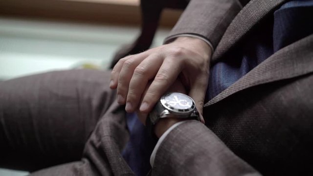 Man in brown suit looking at wrist watches indoors