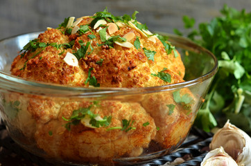 Baked whole cauliflower in a glass casserole. Parsley on cauliflower