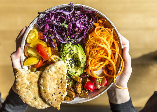 Girl holding veggie bowl with tomato, tofu, red cabbage, avocado, carrot, red radish, cress, black sesame and pita bread