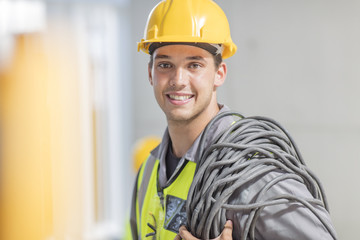 Portrait of smiling electrician with cable on construction site
