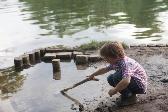 Little boy playing with a stick in the water of a lake