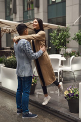 Girl with guy romantically hugging on building background.