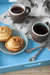 Tasty buns with jam and two cups of tea on a blue wooden background. Next there are two spoons and a light linen napkin.
