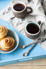 Tasty buns with jam and two cups of tea on a blue wooden background. Next there are two spoons and a light linen napkin.