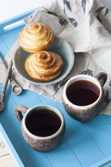 Tasty buns with jam and two cups of tea on a blue wooden background. Next there are two spoons and a light linen napkin.
