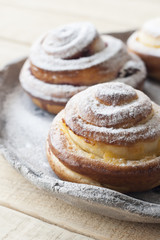 Tasty buns are sprinkled with sugar powder on a light hand-made plate on a light wooden background.