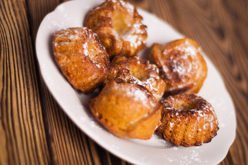 Baked cupcakes sprinkled powdered sugar on white ceramic dish on old rustic brown weathered table