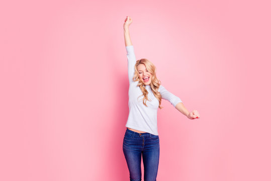 Portrait of cheerful funny girl with arms up celebrating victory, yelling dancing jumping with wide open mouth isolated on pink background