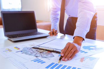 Young businessman holding pen pointing to graph and chart in the office. Accounting and finance Concept.