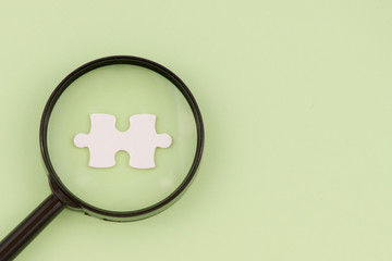 magnifying glass searching for missing puzzle pieces on light green background. Copy space.