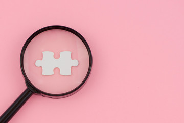 magnifying glass searching for missing puzzle pieces on light green background. Copy space.