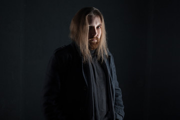 Portrait of man with long hair and beard in black clothes on dark background