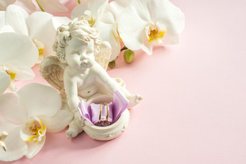 White Orchid angel sculpture wedding rings on pink background