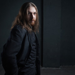 Portrait of man with long hair and beard in black clothes on dark background