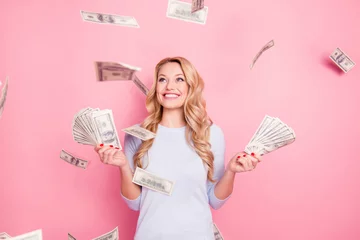Fotobehang Portrait of pretty charming positive cute successful lucky cheerful girl standing under shower from money having a lot of money in hands isolated on pink background © deagreez
