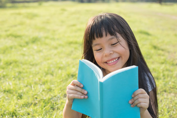 Fototapeta premium Young girl reading a book in a grassy meadow