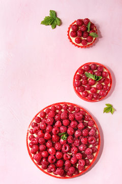 Variety of red raspberry shortbread tarts and tartlets with lemon custard and glazed fresh raspberries over pink pastel background. Top view, space.