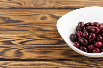 Full white ceramic bowl of red fresh raw dogwood berry on old wooden rustic table with copy space