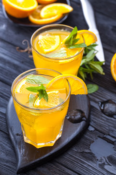 orange cocktail with ice and fresh mint on a black wooden table