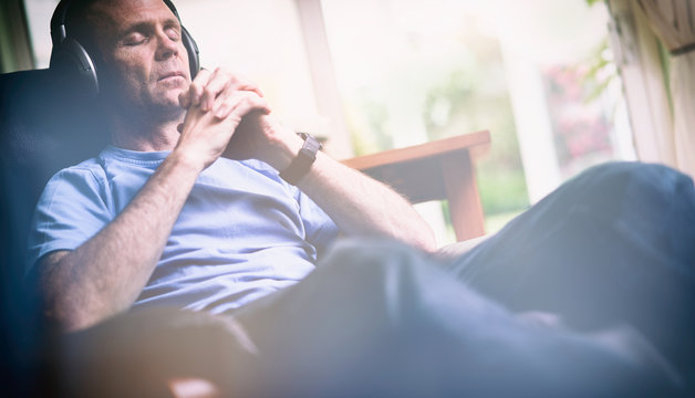 A man enjoying listening to music on wireless headphones in a relaxing armchair. Styling and grain effect added to image.