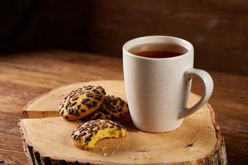 White cup of tea and cookies on a log over country style wooden background, close-up, selective focus