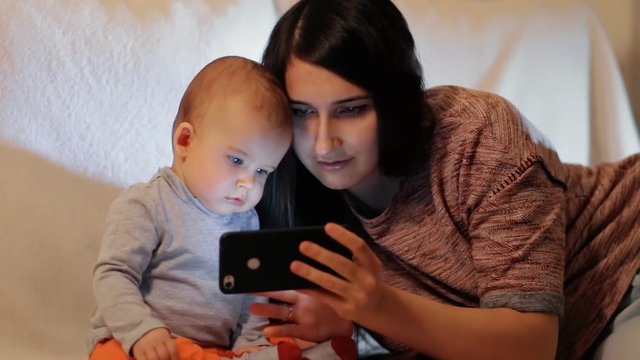A young woman and her little son are watching something carefully on the smartphone screen slow motion shot.