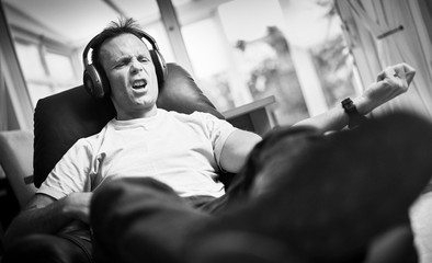 A man enjoying listening to music on wireless headphones in a relaxing armchair. Styling and grain...