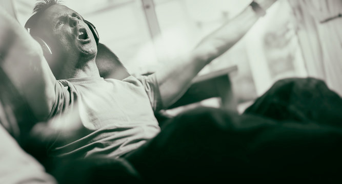 A man celebrating a goal while listening to his favourite team on wireless headphones in a relaxing armchair. Styling and grain effect added to image.