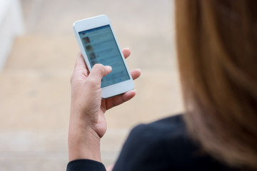 Business women are playing mobile phone, sitting on a bench in the city.