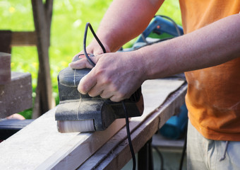 Handyman using electric sander machine outdoors.