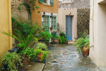 Fototapeta na wymiar Pretty old houses with colorful shuttered windows in a quaint village in Collioure, France. Colorful yellow, blue balconies and doors and green plants near traditional style stone buildings.